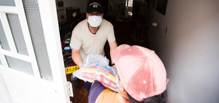 Voluntaria entregando bolsas de leche a ciudadano en la puerta de su casa Familias de Engativá hoy recibieron las ayudas alimentarias con el apoyo de lácteos la Alquería